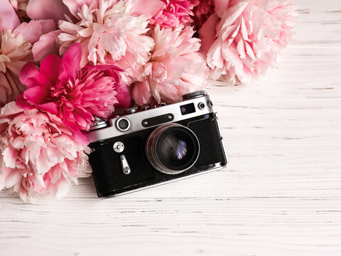 Vintage retro camera and a bouquet of peonies on a white wooden background. International day of the photographer