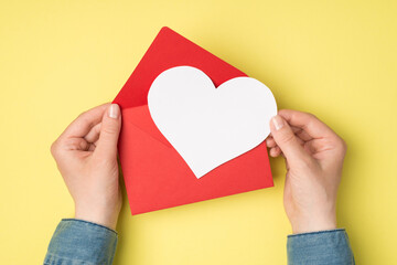 First person top view photo of woman's hands holding open red envelope and white heart on isolated...