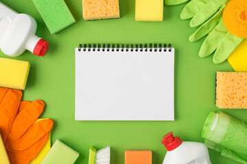 Top view photo of open copybook in the middle detergent foam bottles rubber gloves napkins scouring pads brush and garbage bags on isolated green background with copyspace