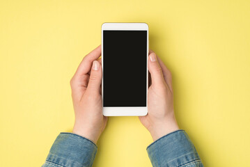 Fototapeta na wymiar First person top view photo of woman's hands holding smartphone display on isolated yellow background with blank space