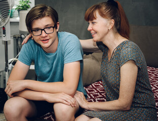 Photo of family relationships. Mom hugs her son at home while sitting on the sofa with a smile - 443200348