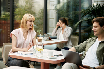Happy businesswoman talking to male colleague while working in a cafe.