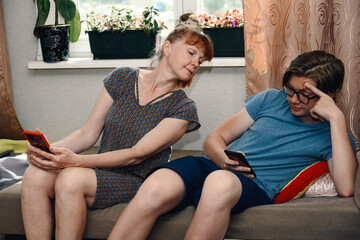 Photo of ordinary family relationships. Mom and teen look at the phone of their son at home while sitting on the sofa - 443200504