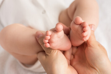 Obraz na płótnie Canvas Closeup photo of mother's hands holding baby's tiny feet on isolated white cloth background
