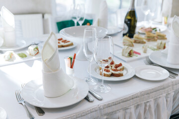 Table setting for a banquet or celebration. Empty wine glasses for spirits, champagne and juice. Set the table. Cloth napkins on a platter. Banqueting hall. Cold appetizers and salads