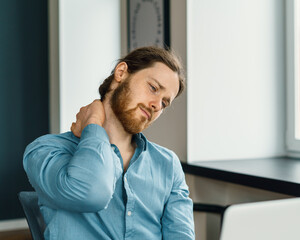 Young tired exhausted businessman suffering from pain in neck during long working day in office,...
