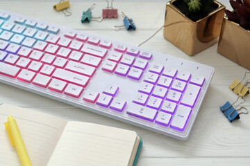 Modern RGB keyboard and office stationery on white wooden table