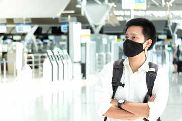 Asian traveler man wearing face mask waiting to board into airplane, standing in departure terminal in airport