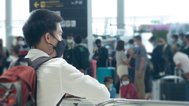 Asian traveler man wearing face mask waiting to board into airplane, standing in departure terminal in airport