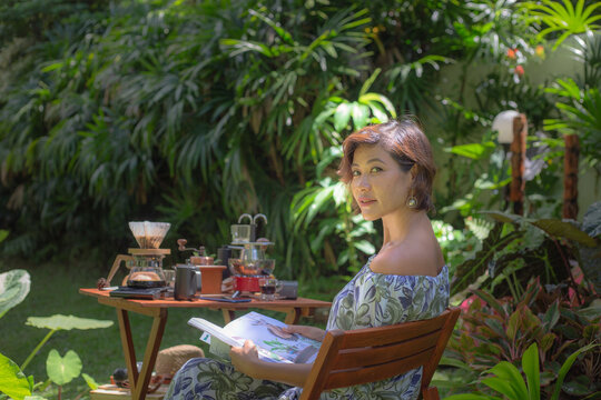 ThailandA woman drink hot coffee in green garden. .A woman relax in green garden with coffee set on wooden table. .green garden background.