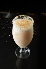 bartender special cold peanut or almond cocktail mocktail with fresh coconut milkshake juice in tall glass goblet on black background luxury hotel pub iced beverage menu