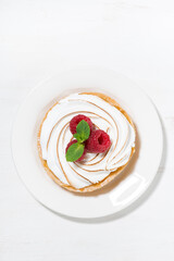 sweet tartlet with meringue and raspberry on white plate, vertical top view