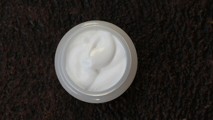 A white jar with white cream on a rustic earthy background. Medicinal, herbal or cosmetic