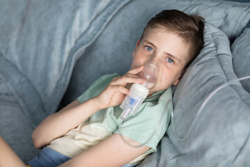 Cute boy with blue eyes doing inhalation with a nebulizer at home