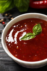 Spicy chili sauce with basil on dark wooden table, closeup