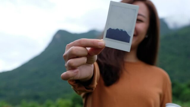 A female traveler showing a polaroid picture of a beautiful greenery mountain while traveling in the forest
