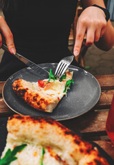 woman hands with knife and fork cutting pizza on table in cafe outdoor