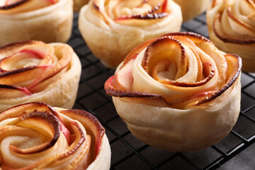 Obraz na płótnie Canvas Cooling rack with freshly baked apple roses on grey table, closeup. Beautiful dessert