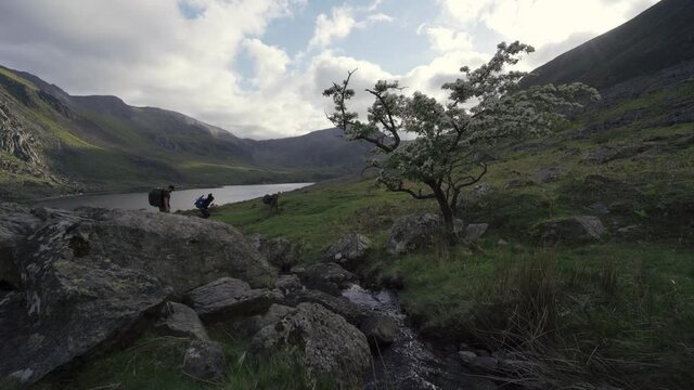 A man with children hiking through Snowdonia over a mountain stream
