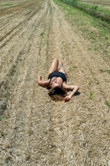 Young girl lying on the hay on the field on summer day, sunbathes