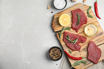 Fresh raw meat steaks and spices on light grey table, flat lay. Space for text