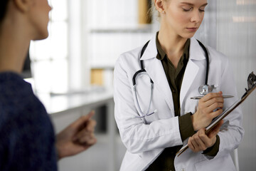 Friendly smiling female doctor and patient woman discussing current health examination while...