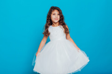 Fototapeta na wymiar Beautiful little curly girl 5 years old in a white dress on a blue background