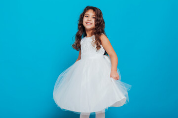 Beautiful little curly girl 5 years old in a white dress on a blue background