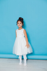 Beautiful little girl dances to the song in a white dress on a blue background