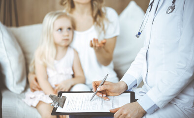 Obraz premium Doctor and patient. Pediatrician using clipboard while examining little girl with her mother at home. Sick and unhappy child at medical exam. Medicine concept