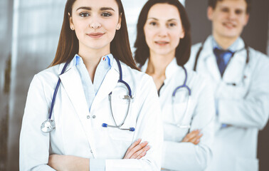 Fototapeta premium Group of young professional doctors is standing as a team with arms crossed in a hospital office and is ready to help patients. Medical help, insurance in health care, best disease treatment and