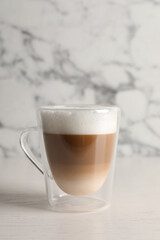 Glass cup of delicious layered coffee on white table against marble background, space for text
