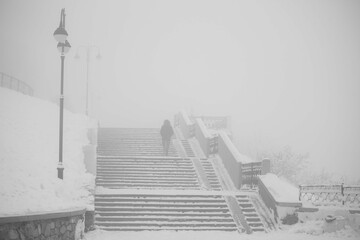 a lonely man climbs the stairs in a snowy city during a heavy snowfall