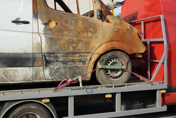 one big burnt car a minibus stands on a tow truck on the street