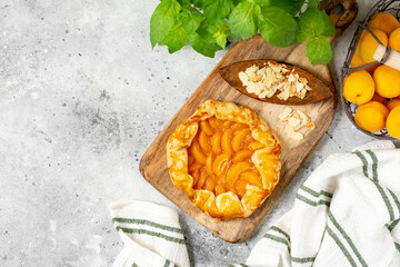 French Galette or a pie with apricots and almonds on on a wooden serving board on a light gray culinary background top view. Summer homemade sweet pastries