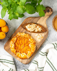 French Galette or a pie with apricots and almonds on on a wooden serving board on a light gray culinary background top view. Summer homemade sweet pastries