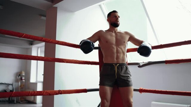 The trained young man, with a fighting spirit, sits on the corner of the ring, being prepared for the fight. Maximum intensity exercise. Healthy lifestyle. Sport concept