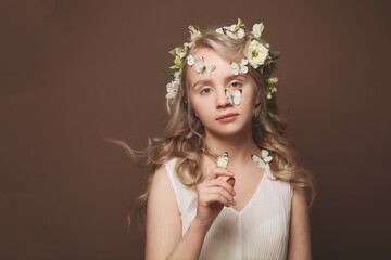 Fashion art portrait of woman in summer dress and white flowers holding butterfly in her hand. Windy curly hair, natural nude makeup