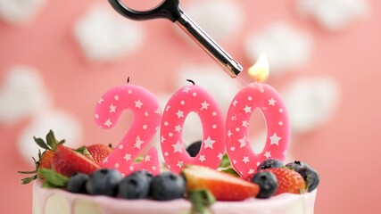Birthday cake candle number 200. Candle and cake on pink background and fire by lighter. Close-up and slow motion