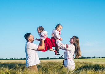 A family in a poppy field dressed in a national Slavic costume. Mom, dad and twin girls in embroidered shirts frolic on sunny day. Concept of a happy childhood, history and togetherness with ancestors