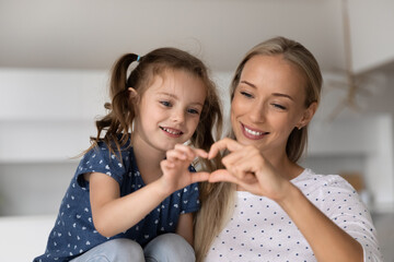 Smiling loving mother with adorable little daughter showing heart gesture, joining hands fingers,...