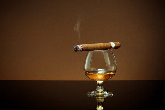 close up view of glass of cognac with cigar on top on color back. 