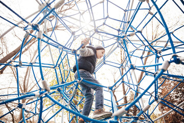 Little boy plays in the playground on the rope road