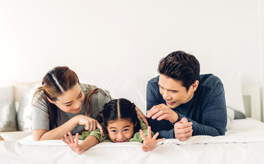 Portrait enjoy happy smiling love asian family father and mother with young parents little child asian girl daughter play and looking together in moments good time lying on the bed at home