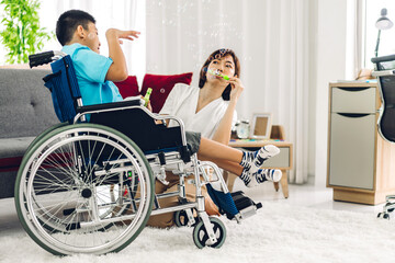 Fototapeta na wymiar Portrait of enjoy happy love family asian mother playing and carer helping look at disabled son child sitting in wheelchair moments good time at home.disability care concept