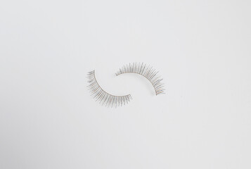 Two false eyelashes against plain white background with space for copy
