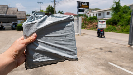 Asian delivery man holding a black plastic wrap in front of a house and the recipient of the box from the delivery man