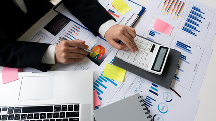 The accountant uses a calculator and a computer with a pen in hand. Finance in progress and calculated in expense table and on table with graph concept of finance with top view
