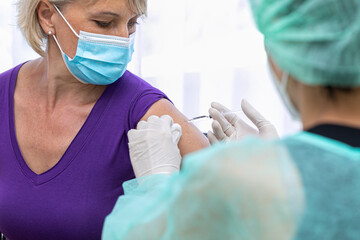 Medical Nurse in Safety Gloves and Protective Mask is Making a Vaccine Injection to a Female...