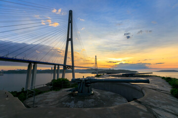 Russian bridge across the Eastern Bosphorus Strait in Vladivostok. Combat guns of the Novosiltsevskaya battery against the background of the Russian bridge. Fortification structures of Vladivostok.